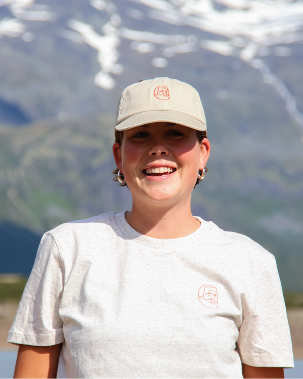 Person wearing a cap and t-shirt with a logo, standing in front of mountains